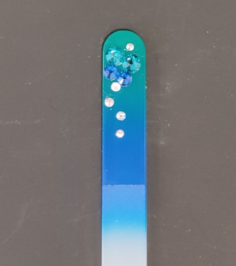 Nagelvijl met blauwe Swarovski steentjes op een blauw/groene achtergrond